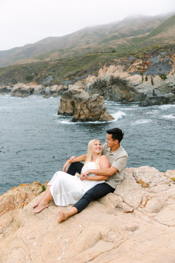 couple cozying up in Big Sur against crashing waves